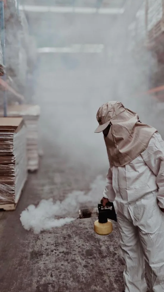 Técnico con traje de protección fumigando una bodega